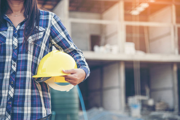 Woman engineer working on construction site and holding yellow hard hat safety helmet head protection at manufacturing industry. Construction Concept. - Photo, image