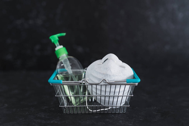 essential items grocery shopping and how stay safe during virus outbreaks like covid-19 at the store, shopping basket with face mask and hand sanitizer for protection from contagion - 写真・画像