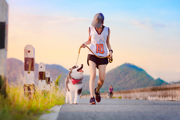 Kadın köpek yavrusuyla günlük egzersiz yapıyor, parktaki yolda koşuyor.  - Fotoğraf, Görsel