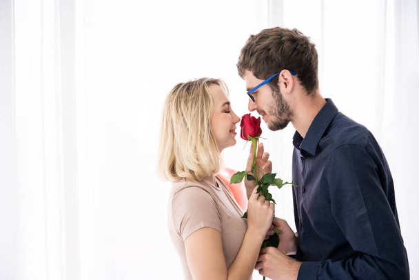 Lovely young caucasian couple in romantic moment together. Husband giving the beautiful red rose to his wife in valentines day. Valentines day and togetherness concept with copy space. - Фото, зображення