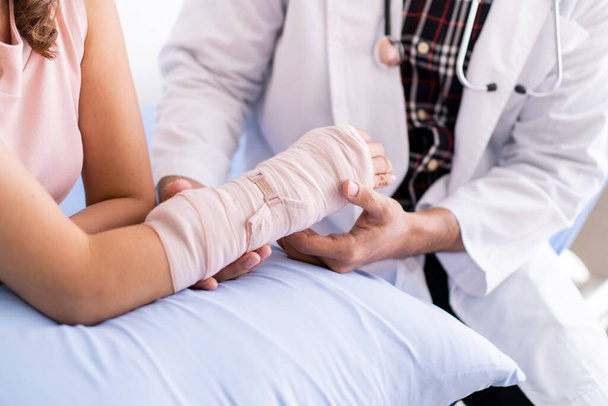 骨の専門医は腕に深刻な怪我をした女性をスプリットと包帯で調べています。病院で腕を骨折した女性患者と話す医師。負傷者の概念の治癒. - 写真・画像
