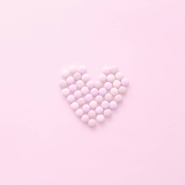 Candies forming a heart shape on pastel background - Foto, afbeelding