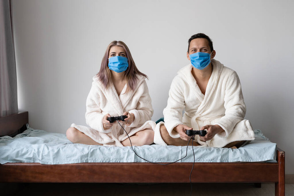 兄と妹はコンピュータゲームをしてる隔離中にトリックと修正されたジョイスティックを使って。顔には保護医療用マスクが着用されています。covid-19との戦い。テキストの場所 - 写真・画像