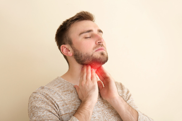 Hombre joven comprobando la glándula tiroides en el fondo de color
 - Foto, Imagen