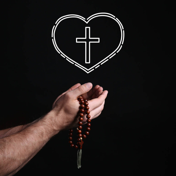 Mannelijke handen met rozenkrans kralen, kruis en hart op zwarte achtergrond - Foto, afbeelding