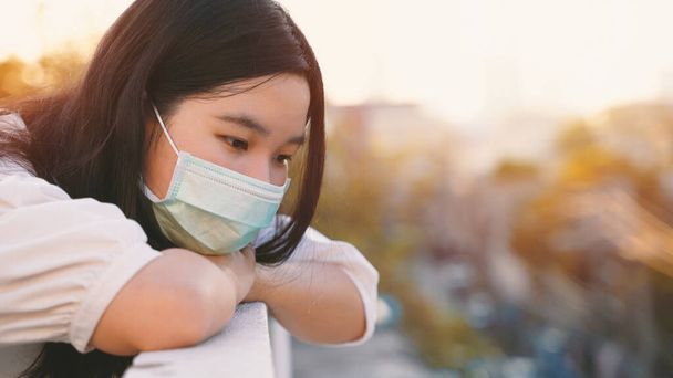 Jeune femme de génération z asiatique sur le toit se sentant ennuyée et regardant le paysage urbain tout en portant un masque, en se mettant en quarantaine ou en restant à la maison pendant la COVID-19 et la pandémie de coronavirus - Photo, image