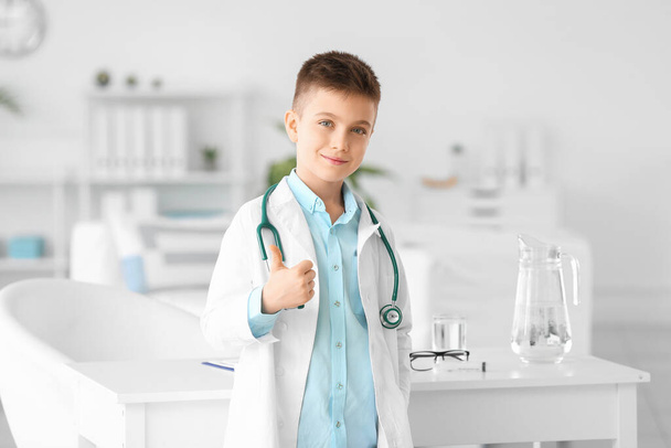 Lindo pequeño médico mostrando gesto de pulgar hacia arriba en la clínica
 - Foto, imagen