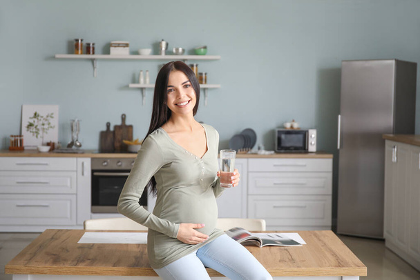 Bella donna incinta che beve acqua in cucina
 - Foto, immagini