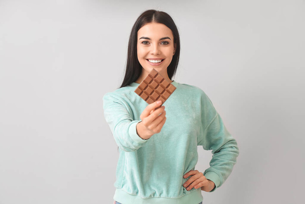 Piękna młoda kobieta ze smaczną czekoladą na jasnym tle - Zdjęcie, obraz