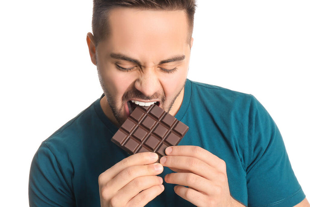 Handsome young man eating tasty chocolate on white background, closeup - Фото, зображення