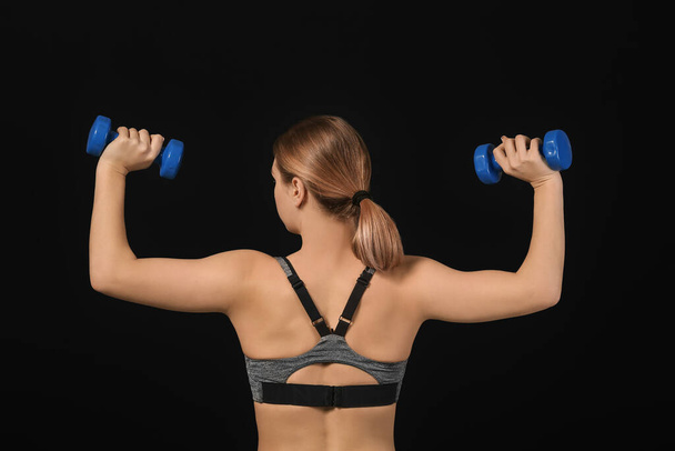 Sporty young woman training with dumbbells on dark background - Foto, immagini