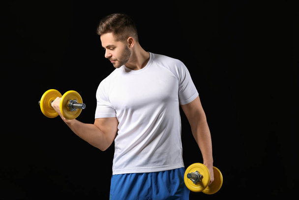 Sporty young man training with dumbbells on dark background - Foto, Bild
