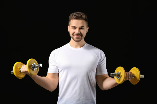 Sporty young man training with dumbbells on dark background - Fotoğraf, Görsel