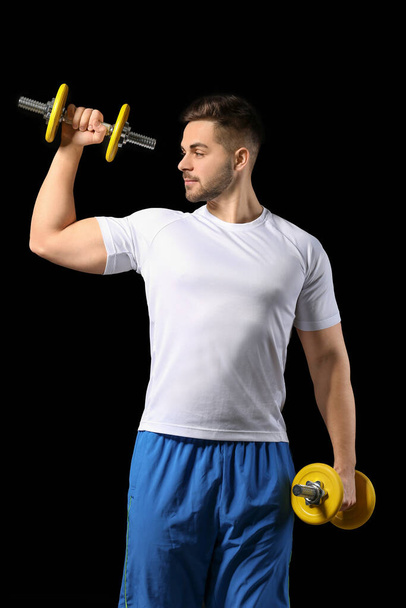 Sporty young man training with dumbbells on dark background - Foto, Imagem