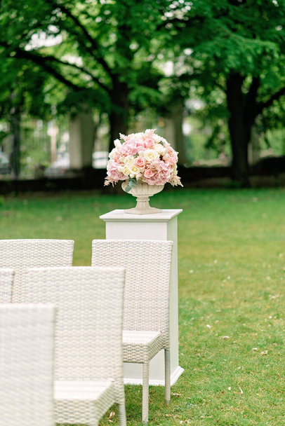 Un beau bouquet de fleurs dans un vase en pierre se dresse sur une colonne sur un fond vert. Décor pour la cérémonie de mariage. Vertical - Photo, image