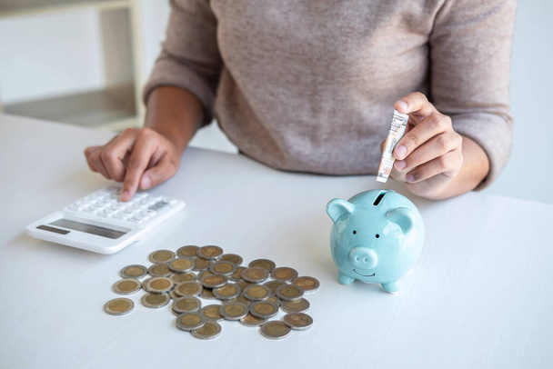 Young woman putting money into piggy bank planning growing saving to strategy and calculating with money box for future plan fund of travel, education, home and retirement. - Foto, Imagen