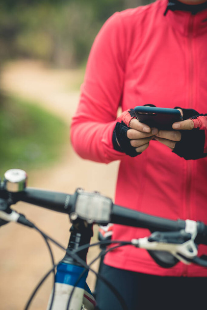 Cyclist use smartphone for navigation when riding mountain bike on forest trail - Zdjęcie, obraz