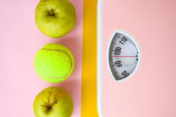 Vihreä omena mittanauhalla ja vaaleanpunaisilla painoasteikoilla. Terveydenhuollon käsite, kunto kotona, ruokavalio
 - Valokuva, kuva