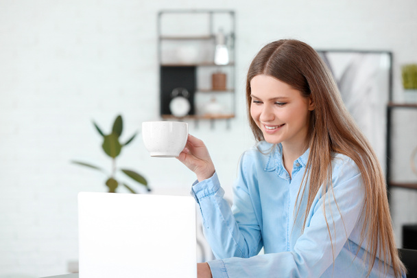 Молода жінка п'є каву під час роботи на ноутбуці в кафе
 - Фото, зображення
