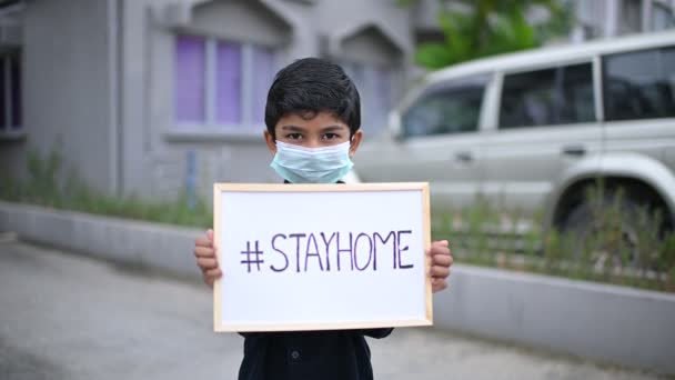 家にいます.コロナウイルスcovid-19感染症.マスクを身に着けているアジアの少年は、図面を表示します"#STAYHOME"病気やほこりを防ぐために,午後5時,自宅の検疫コロナウイルスパンデミック予防に滞在. - 映像、動画