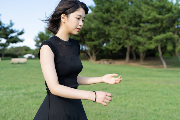 Deniz kenarındaki bir parkta siyah elbiseli Asyalı genç bir kadın. - Fotoğraf, Görsel