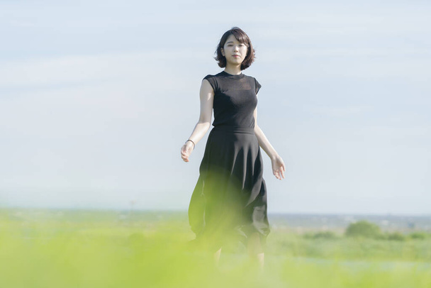 Asian (Japanese) young woman in a black dress in a park by the sea - Foto, afbeelding