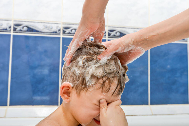 Mom lathers the head of a baby with eyes closed shampoo - Foto, Imagen