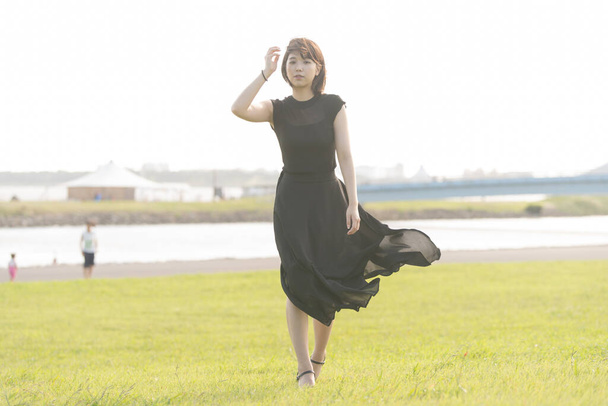 Азійська (японська) молода жінка в чорній сукні в парку біля моря. - Фото, зображення