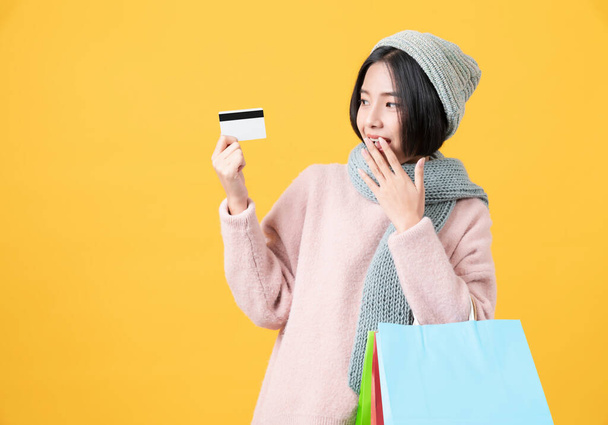 Vidám gyönyörű ázsiai nő gazdaság sokszínű bevásárló táskák és hitelkártya világossárga háttér. - Fotó, kép