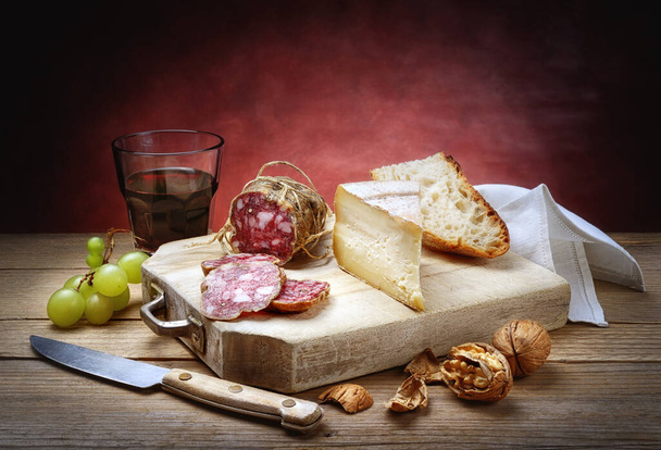 Salami, ser, chleb, winogrona, orzechy włoskie i kieliszek czerwonego wina. - Zdjęcie, obraz
