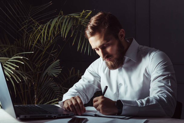 Handsome Thoughtful Bearded Businessman Sitting At His Workplace Writing A Note. Business Theme - 写真・画像