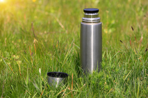 térmica de aço e xícara no prado verde na grama
 - Foto, Imagem
