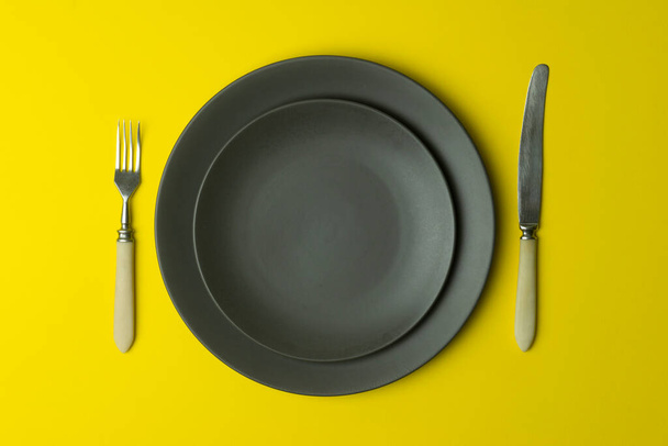 Assiette vide sur fond jaune. Assiette en céramique grise vide avec couteau et fourchette pour la nourriture et le dîner sur fond jaune coloré
. - Photo, image