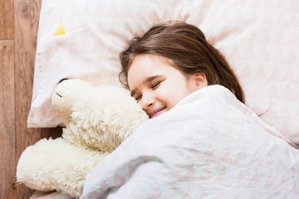 A little girl sleeps on a pillow and takes cover with a blanket, hugs a bear, baby sleep, relaxation, joy, morning, soft toy, family and home - Valokuva, kuva