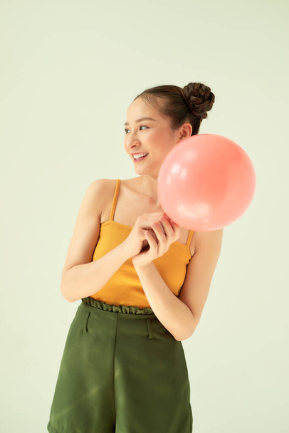 Güzel, neşeli Asyalı genç kız elinde pembe hava balonu ve açık arkaplanda iki çörek saç stili tutuyor.. - Fotoğraf, Görsel