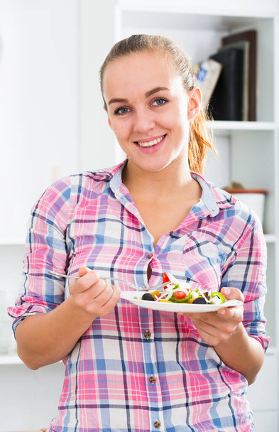 portrait of happy young woman with chestnut hair eating salad at kitchen - 写真・画像