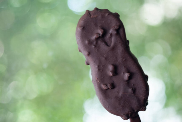 Hände mit Vanilleeis bedeckt mit Schokolade und Nüssen auf Naturhintergrund - Foto, Bild