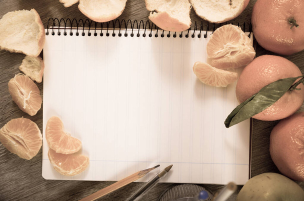 Notebook with empty pages lying amid decoration of tangerines  - Foto, imagen