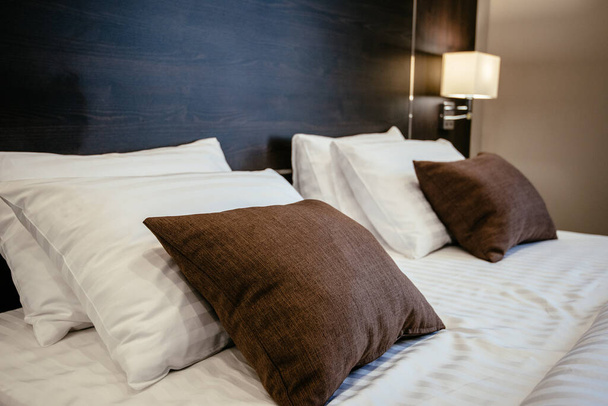 Λευκά και καφέ μαξιλάρια στο κρεβάτι στην κρεβατοκάμαρα, κοντά. Υφάσματα σε ένα σύγχρονο υπνοδωμάτιο. - Φωτογραφία, εικόνα