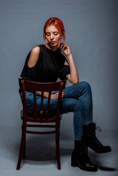 Stylish young woman wearing blue jeans while sitting on cheir in modern studio - Fotografie, Obrázek