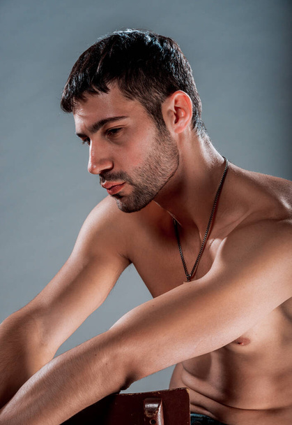 Studio portrait of a shirtless handsome guy sitting on a chair - Foto, Imagen