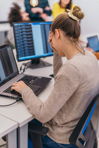 Bild von hinten von einer Mitarbeiterin, die an ihrem Schreibtisch sitzt und an ihrem Laptop arbeitet - Foto, Bild