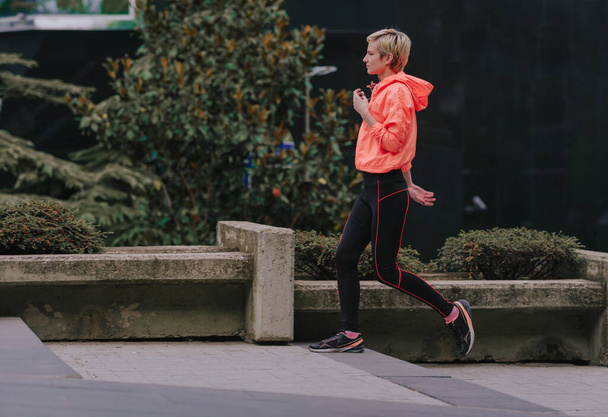 jong aantrekkelijk meisje dragen sportkleding tijdens een run in een stedelijk gebied - Foto, afbeelding