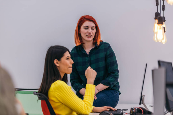 Δύο γυναίκες συνάδελφοι συνομιλούν και χαμογελούν στο γραφείο ενώ κάνουν διάλειμμα. - Φωτογραφία, εικόνα