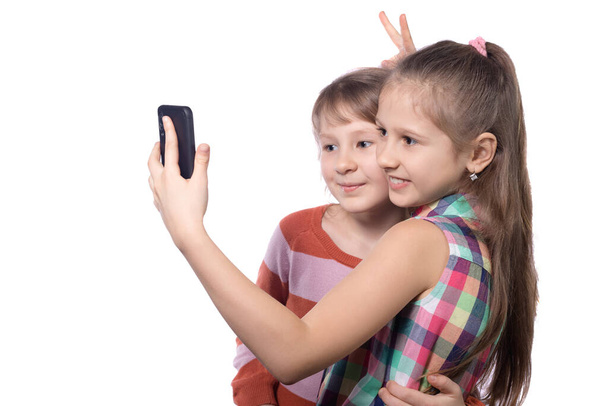 Két aranyos kislány csinál egy szelfit a mobilján. Stúdió fotó elszigetelt fehér háttér. - Fotó, kép