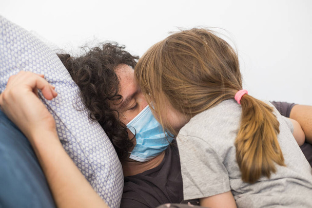 Kaukázusi apa maszkot visel, hogy elkerülje a fertőző csókolózást a kislánnyal a világjárvány idején. Apa és kislánya ölelkeznek.. - Fotó, kép