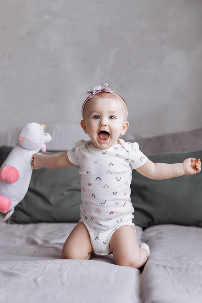 glücklich liebenswertes kleines Mädchen spielt mit Spielzeug Einhorn auf dem Bett zu Hause. Konzept des Kindheitstages. Happy Baby 's, Familientag. - Foto, Bild