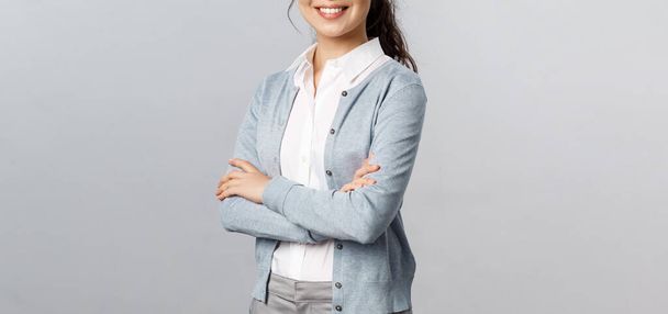 Oktatás, nők és életmód koncepció. Vonzó ázsiai női vállalkozó, lány tutor mosolygós elégedett, keresztbe kéz mellkas, örömmel segít az ügyfél bármilyen kérdés, szürke háttér - Fotó, kép