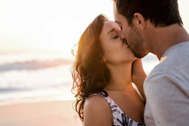 Loving young couple standing in each other's arms and kissing on a sandy beach at dusk - Foto, Imagem