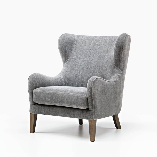 Удобное элегантное кресло из серой ткани с деревянными ножками, расположенное в белой студии - Фото, изображение